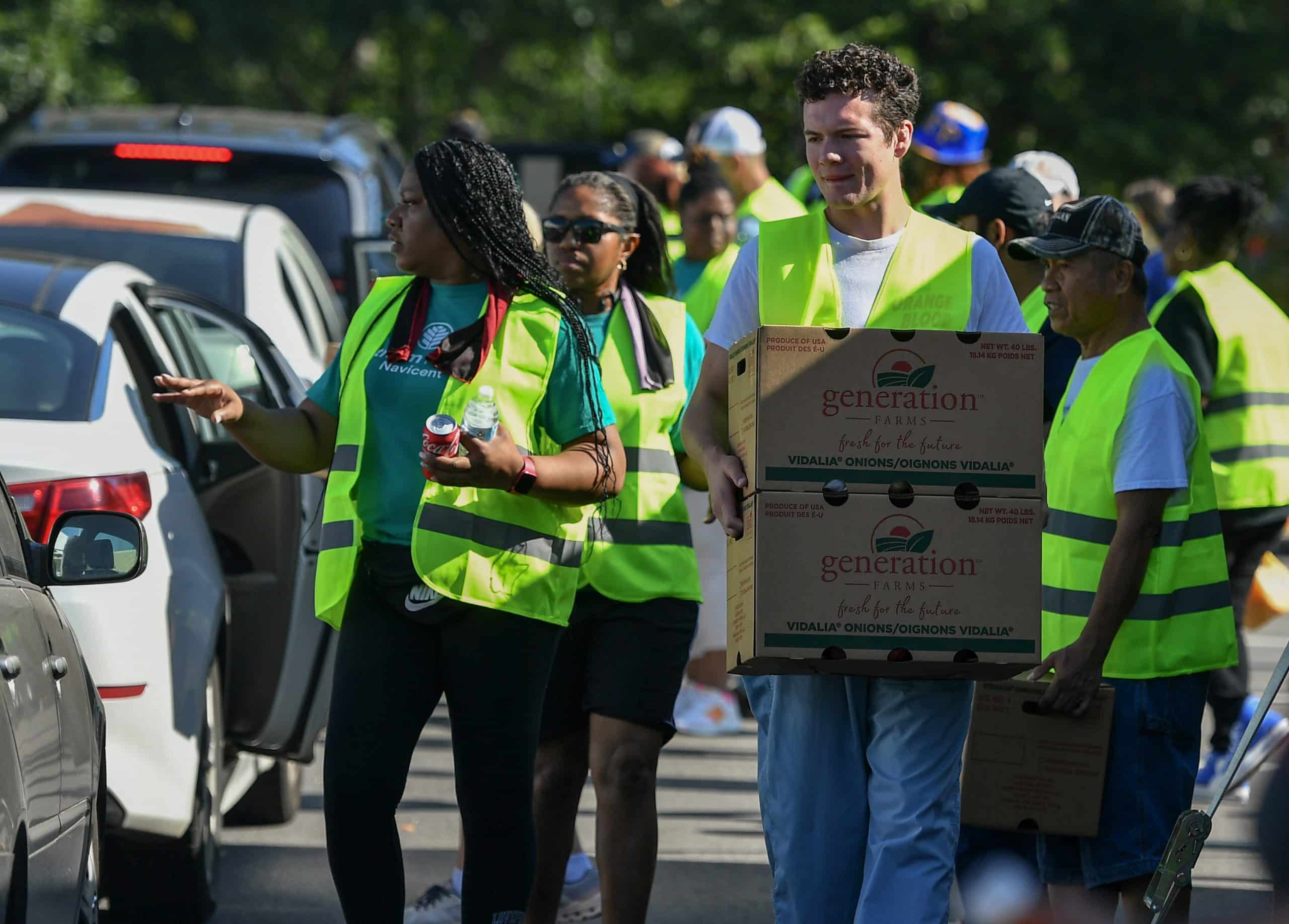 Volunteers carry boxes of to automobiles during a food distribution event.