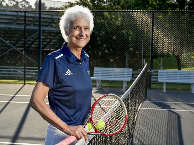 Jaime Kaplan, posing with a tennis racket and ball in Stratford tennis attire on the net of a tennis court.