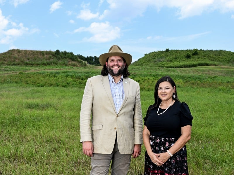 A man and a woman stand outside in front of two mounds covered in grass.