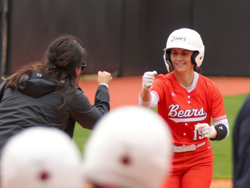 Mercer softball player Hallie Langford, in an orange Bears uniform, fist bumping her coach and smiling as she jogs home.