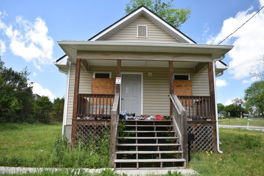 A boarded-up house sits in an overgrown yard.