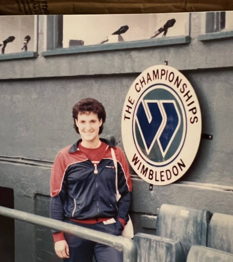 A faded photo of Jaime Kaplan posing in a red-and-blue jumpsuit next to the circular Wimbledon logo.