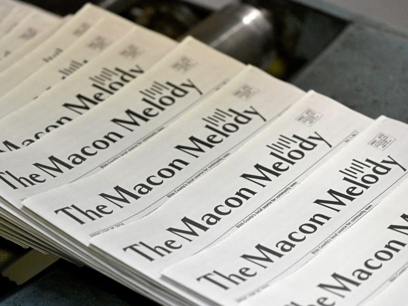 The image shows a stack of newspapers titled “The Macon Melody.” The newspapers are neatly arranged, with the name prominently displayed in bold black letters.