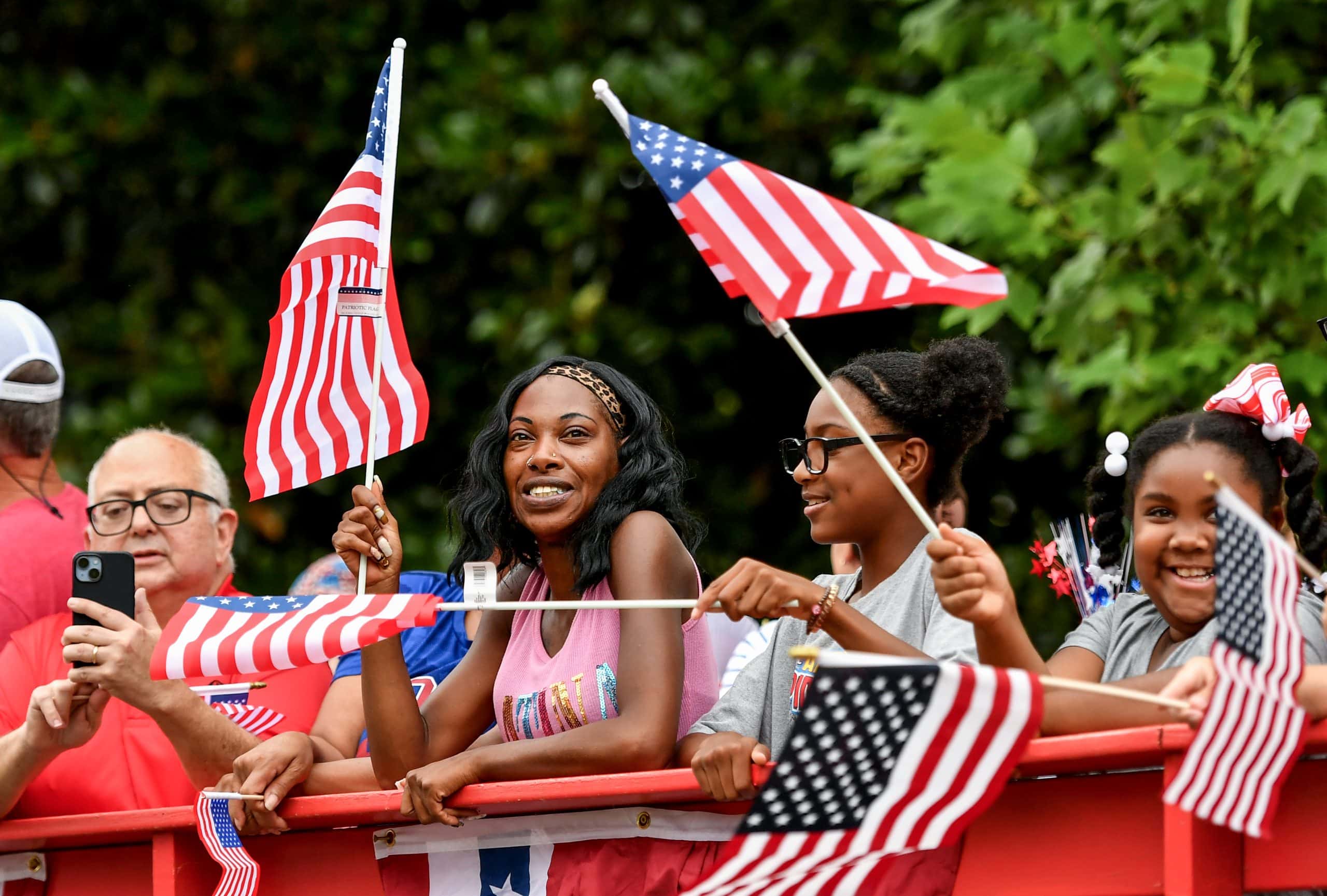 People wave from the a wagon while dressed in patriotic attire while riding down a street.