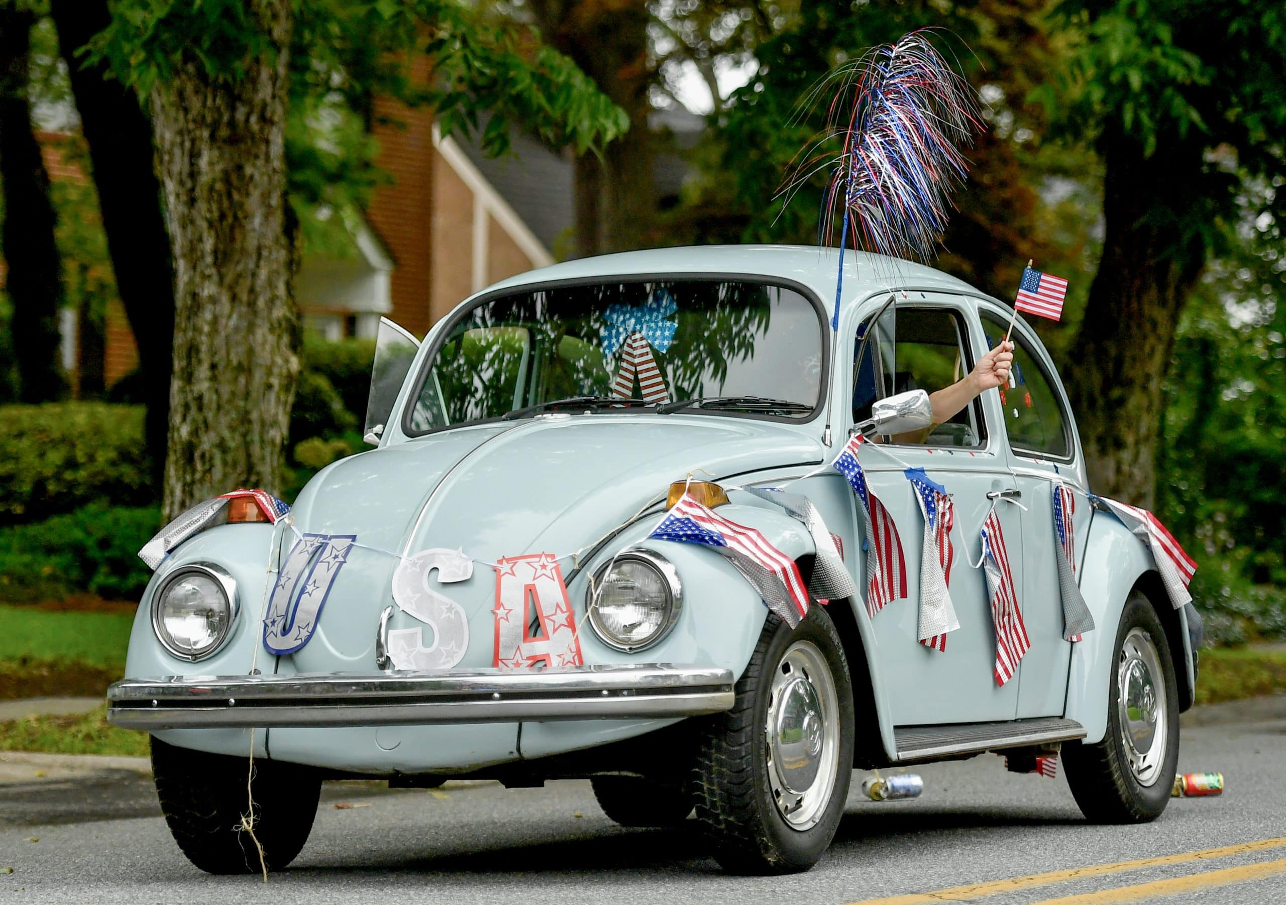 A vintage car covered in patriotic banners rides down a street.