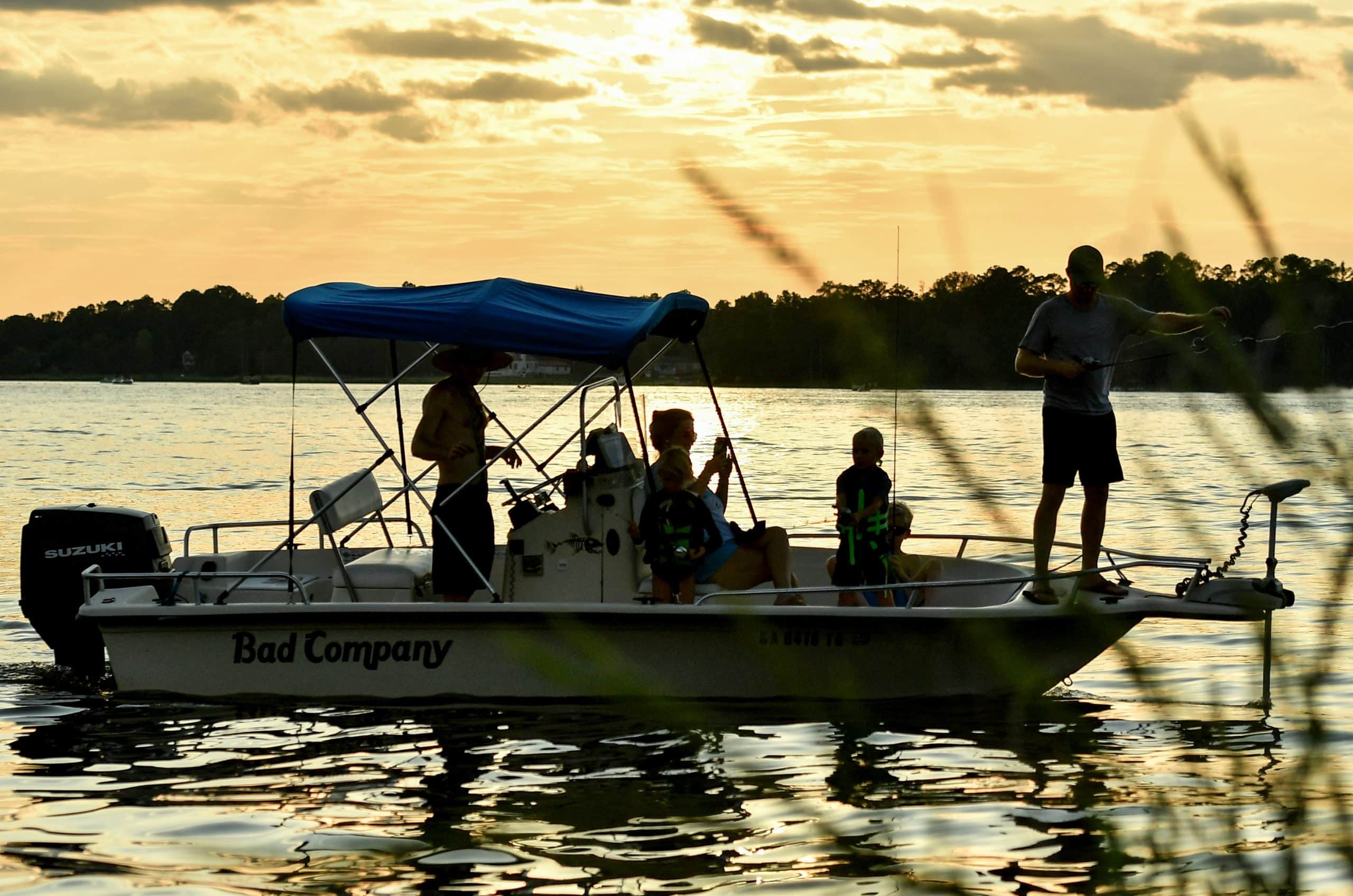 A silhouette of people fishing from a boat along the lake shore.