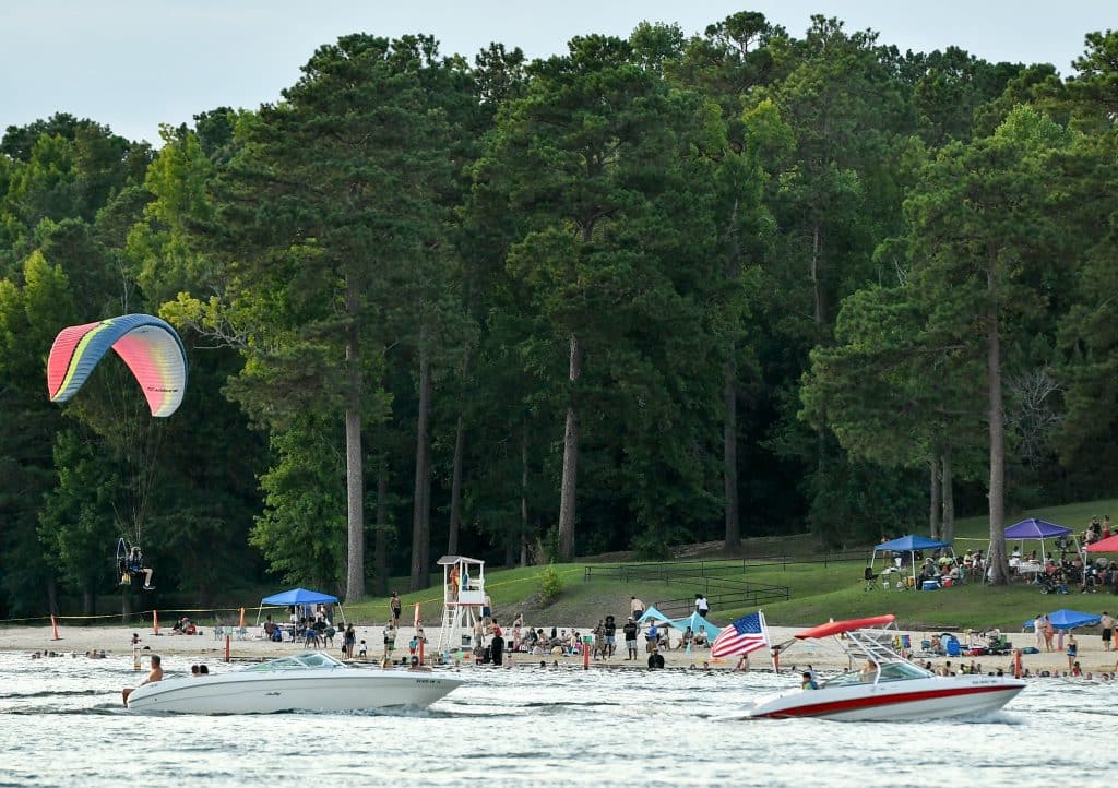 Ski boats ride by a beach along a lake.