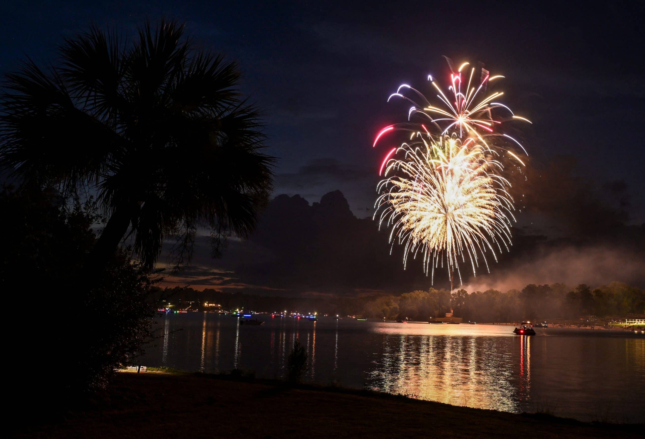 Fireworks go off over a lake.