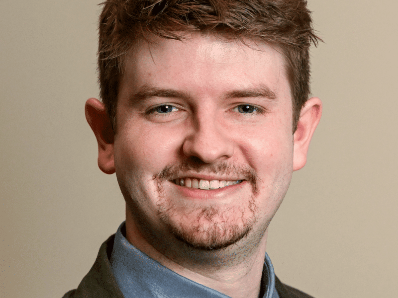 Micah Johnston poses for a standard headshot wearing a green jacket and tie.