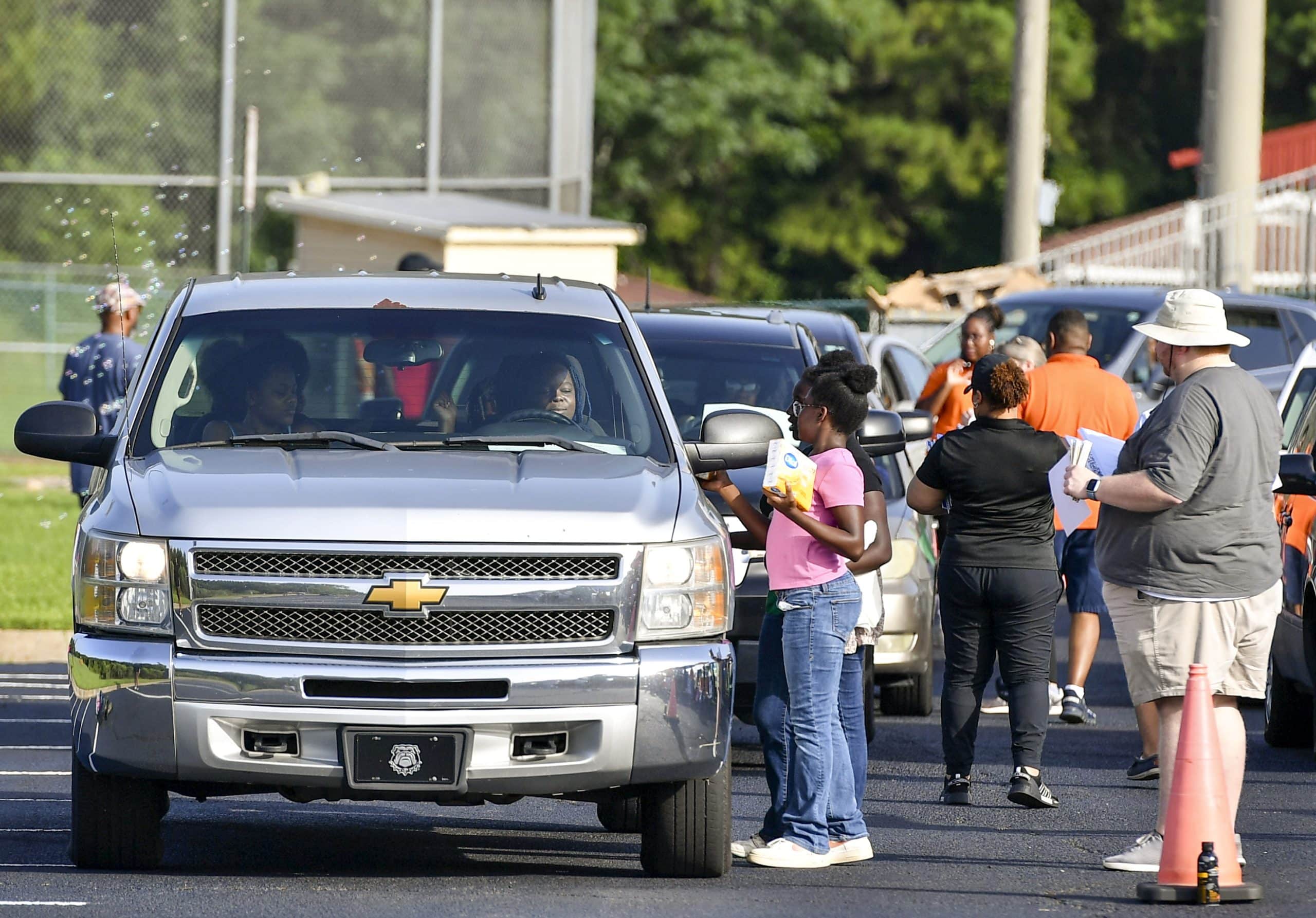 People hand school supplies through windows as automobiles line up in a parking lot.