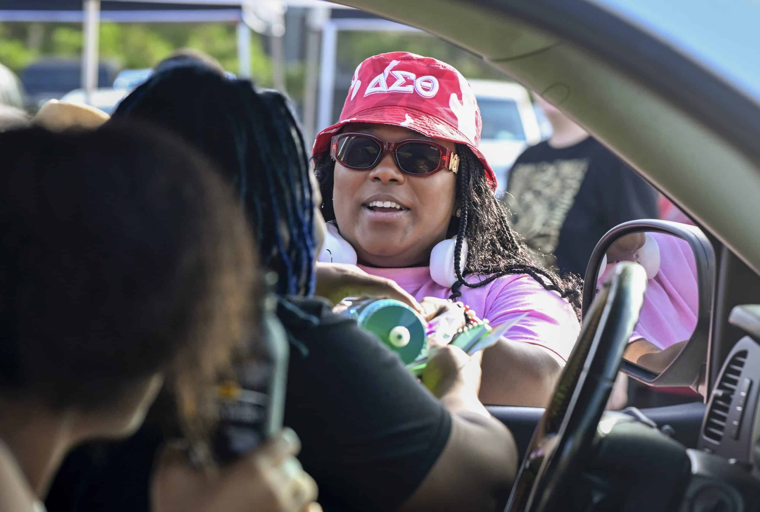 A woman hands school supplies through a car window.