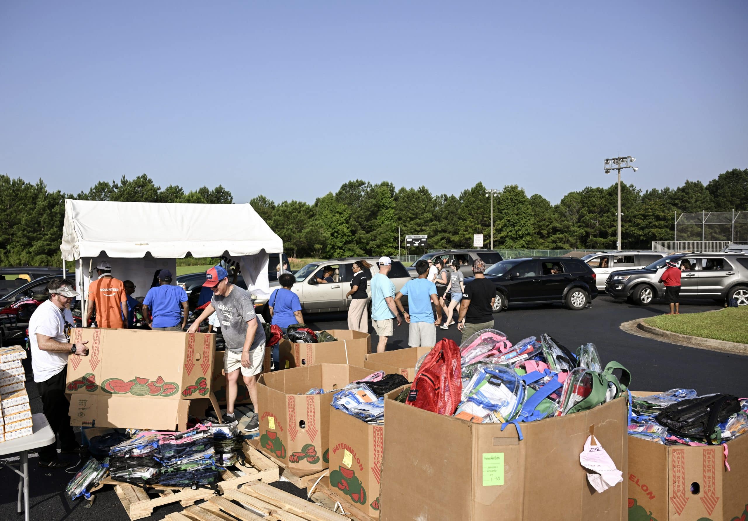 Large boxes filled with backpacks in the foreground as automobiles line up in the background during a school supply giveaway.