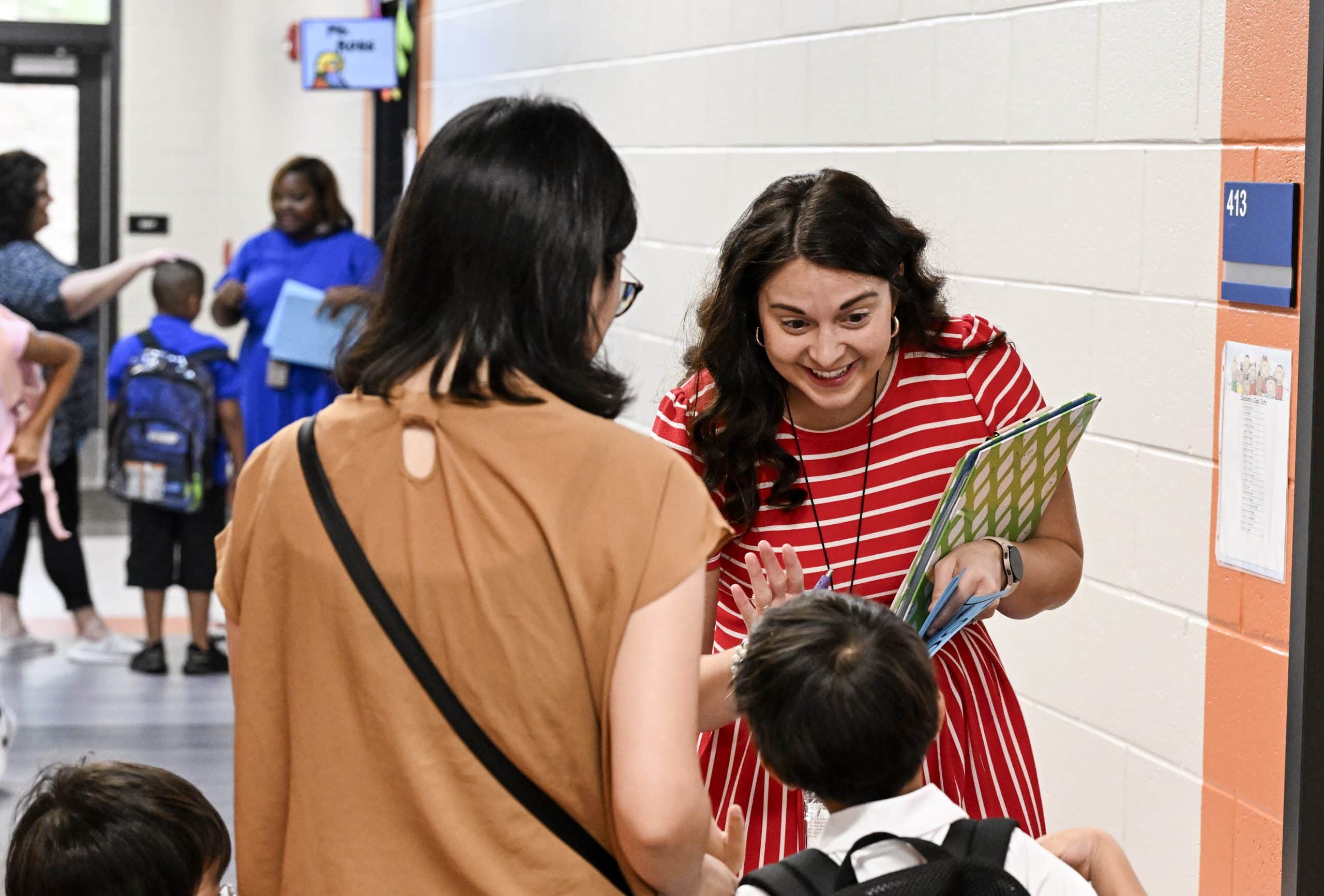A teacher reaches out her hand for a high five from a young student in the hallway of a school.