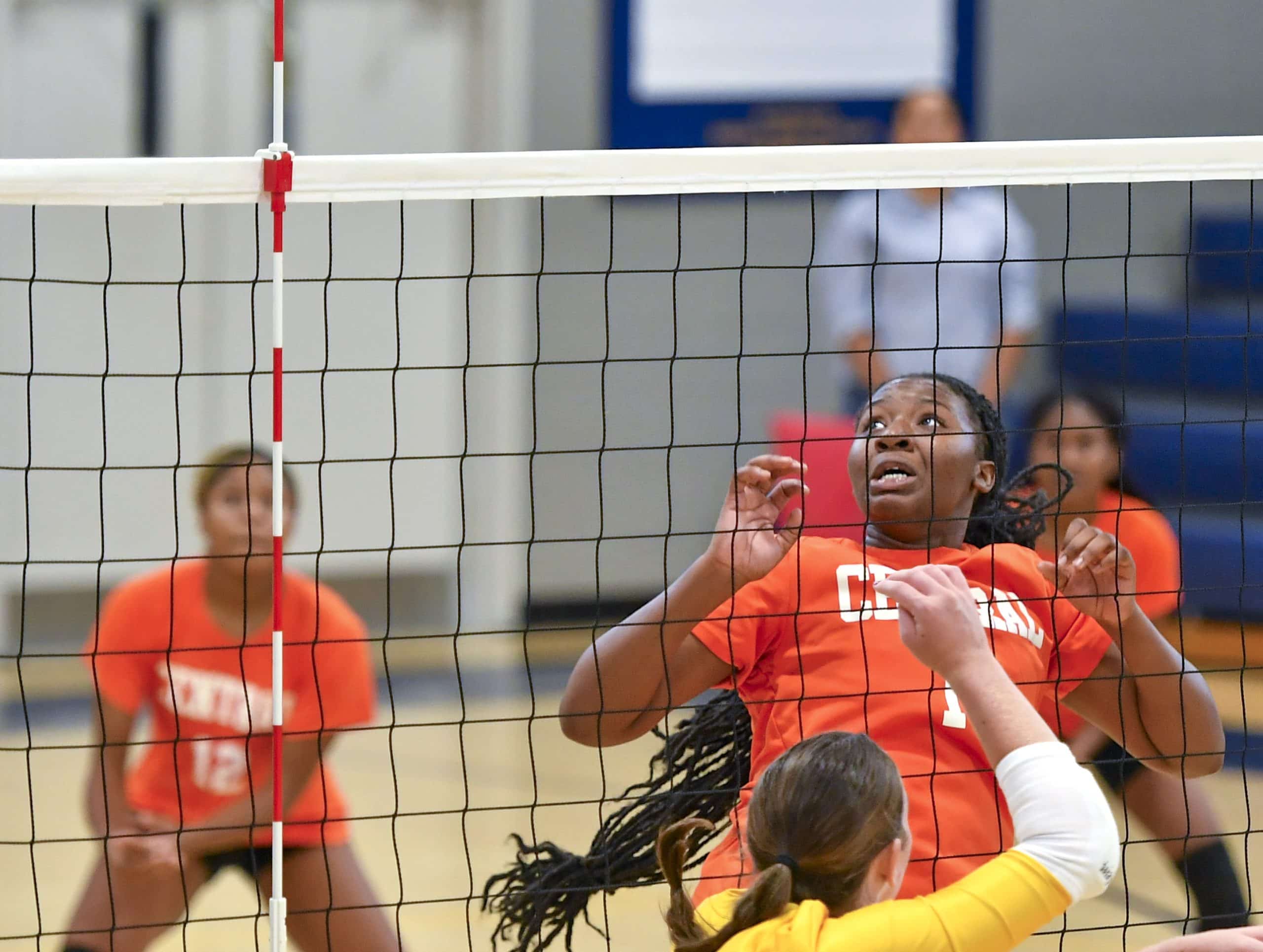 A volleyball player in an orange jersey reacts as the ball (not in frame) goes by her over the net.