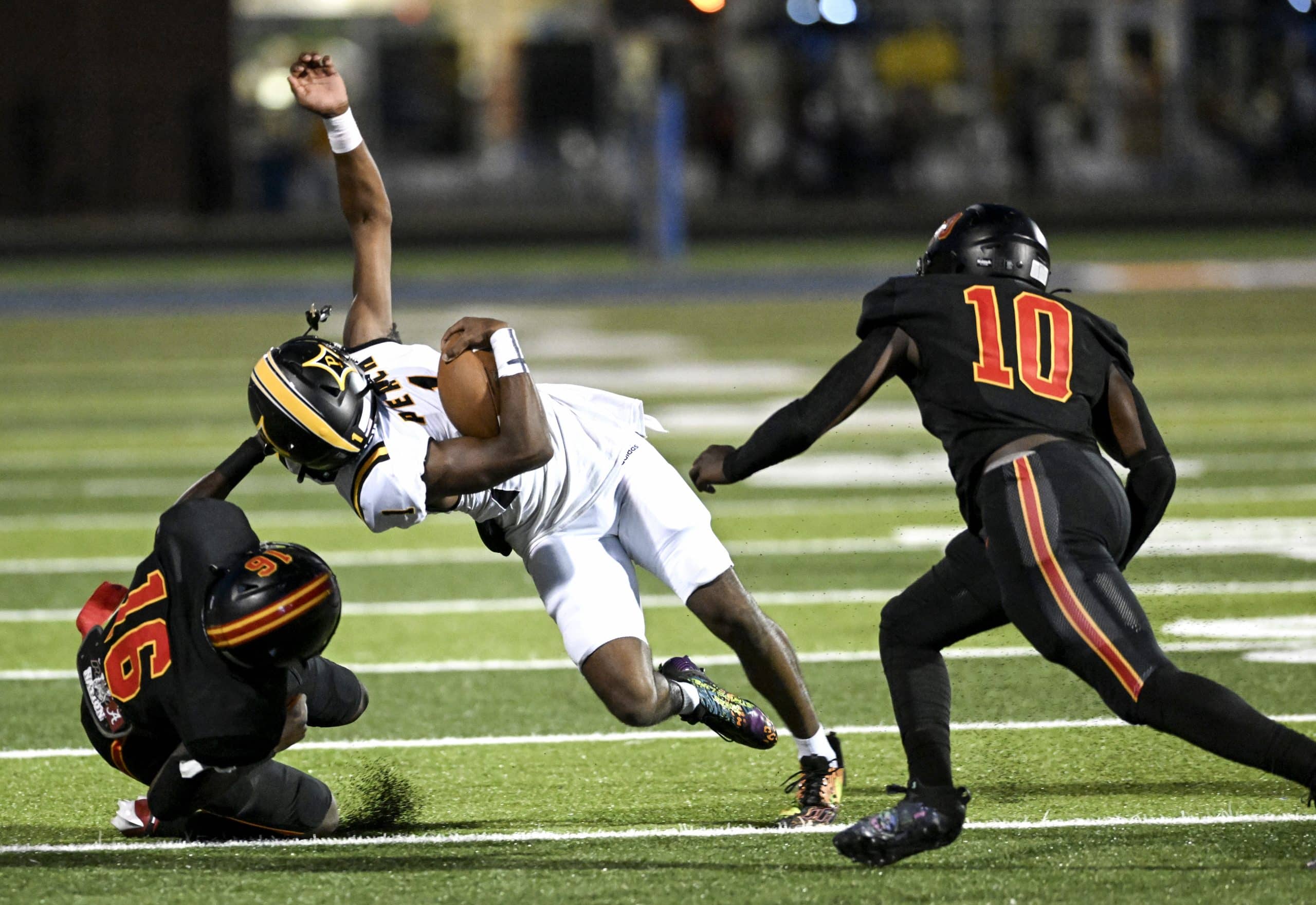 A football player wearing a white uniform is tackled  by a player in a black uniform.