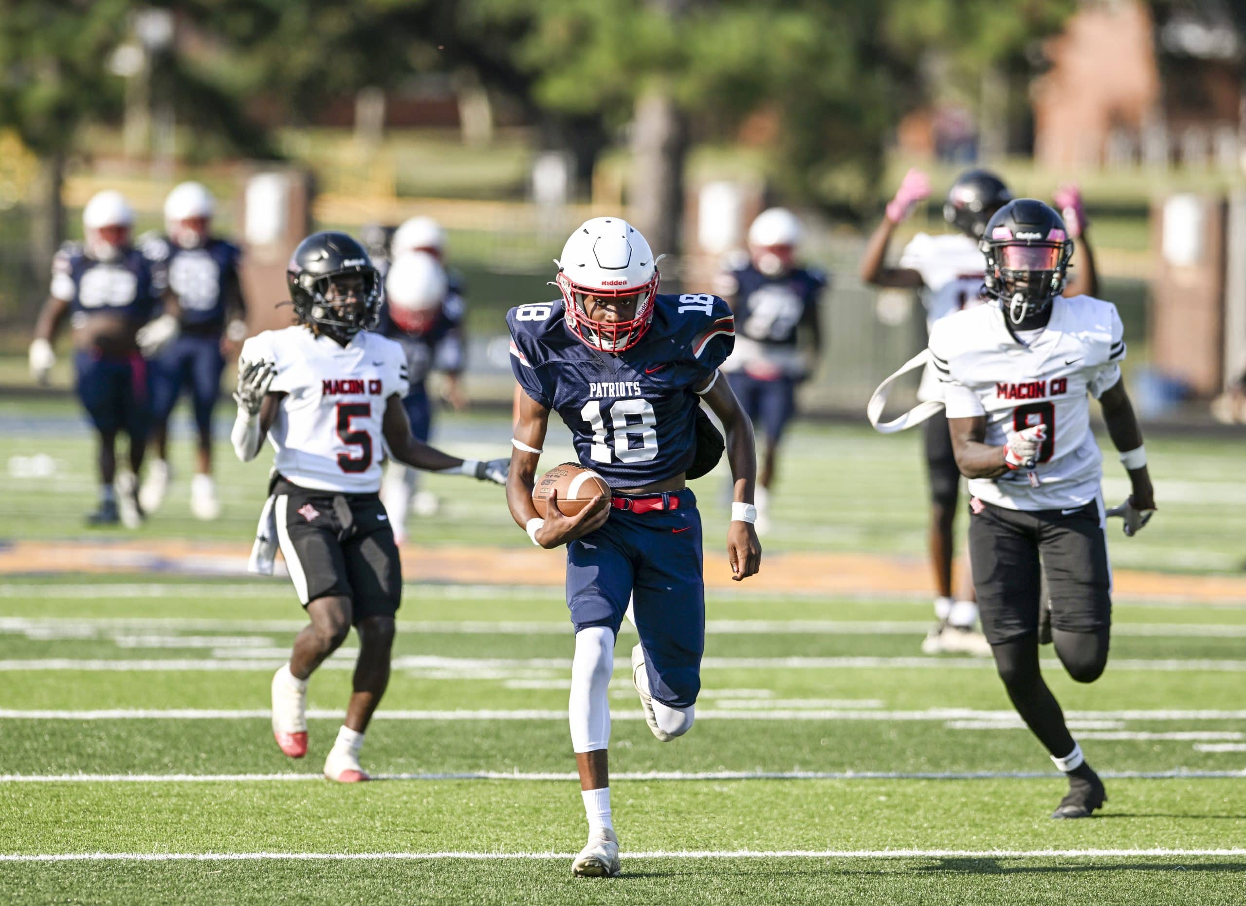 A football player wearing a blue uniform with the number 18 runs between two players in white uniforms.