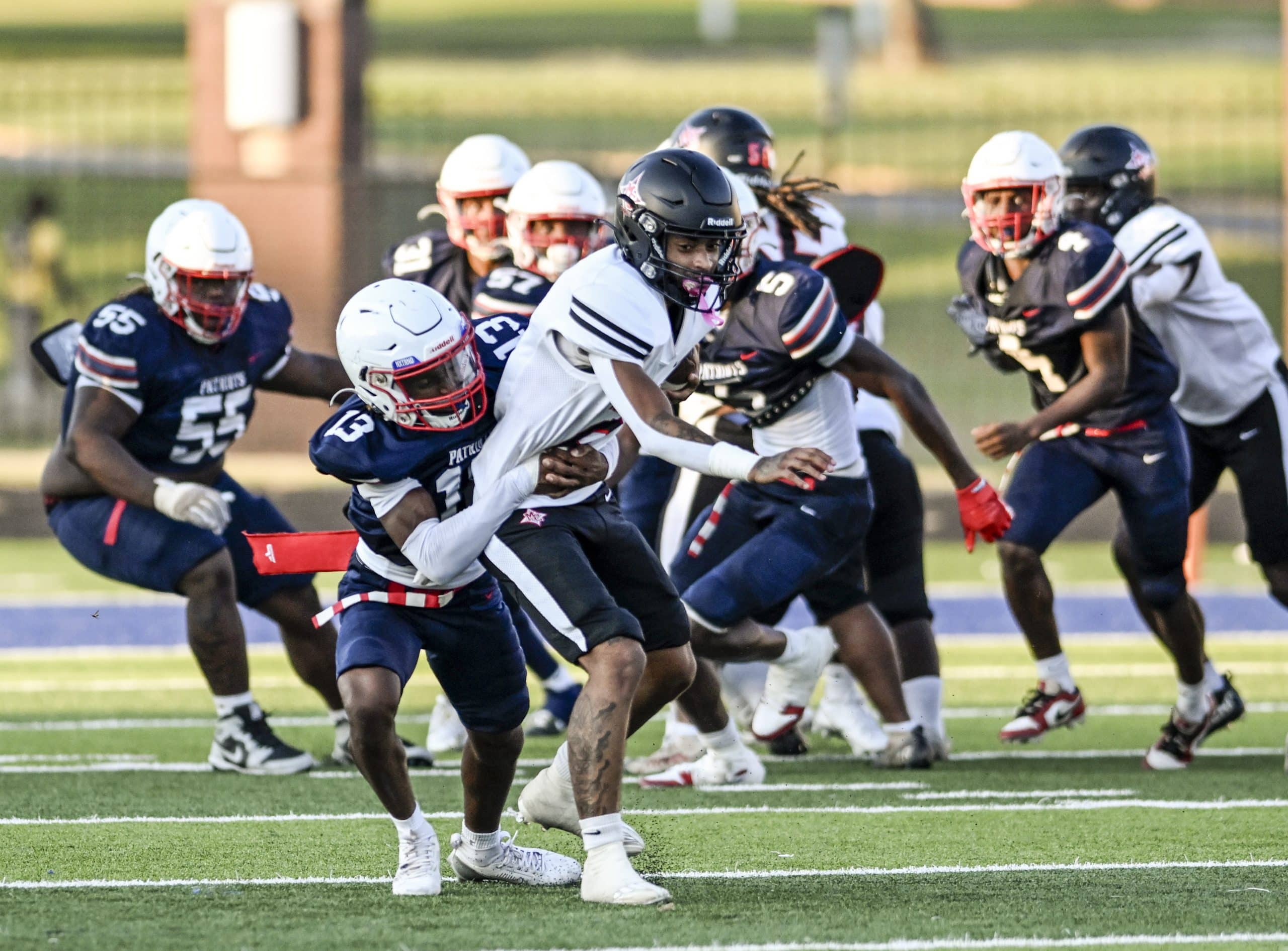 A football player wearing a white uniform with the number 6 is tackled to the ground with the ball by a player in a blue uniform with the number 13.