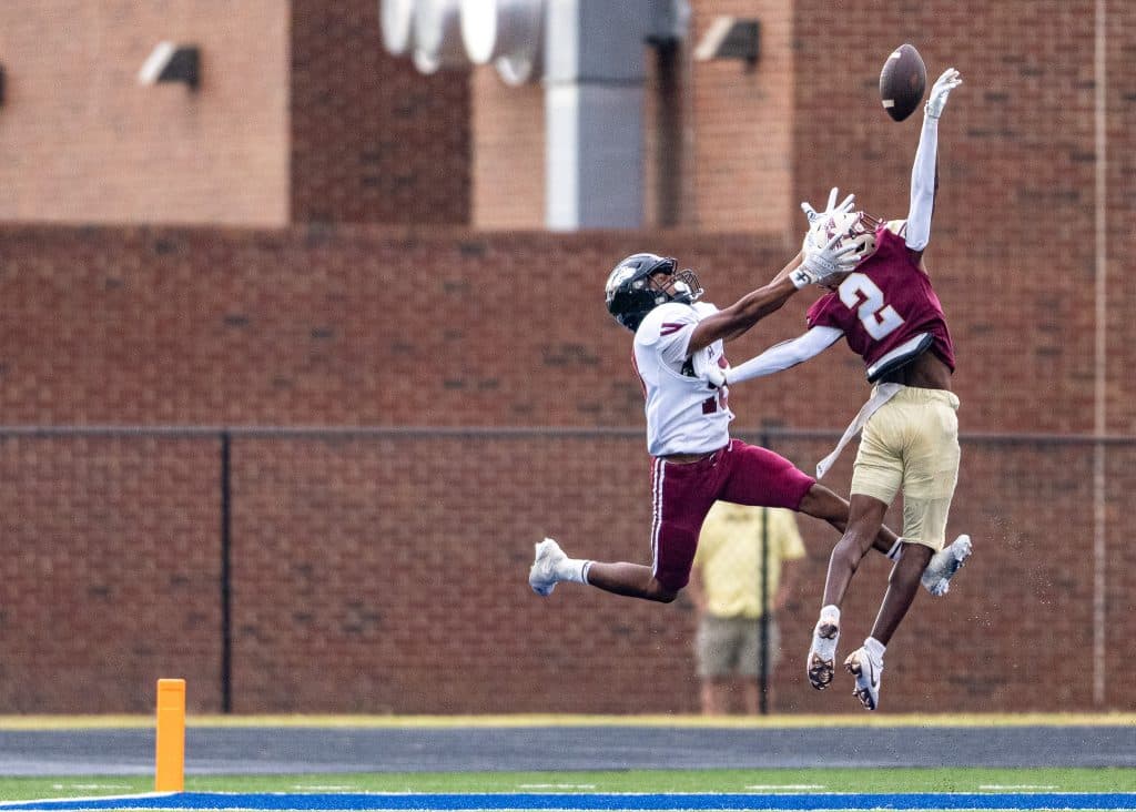 A football player in a garnet uniform with the number 2 breaks up a pass intended for a player in an white uniform with the number 18.