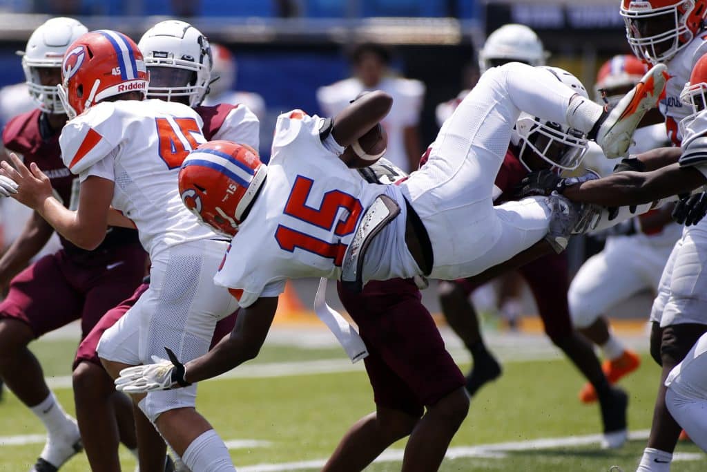 A football player in an all-white uniform with orange numbers, an orange helmet and white gloves is flipped parallel to the ground on a play while holding the ball.